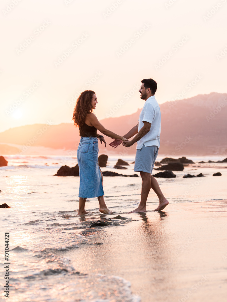 Romantic young couple walking on the beach at sunset, holding hands Romantic young couple walking on the beach at sunset, holding hands