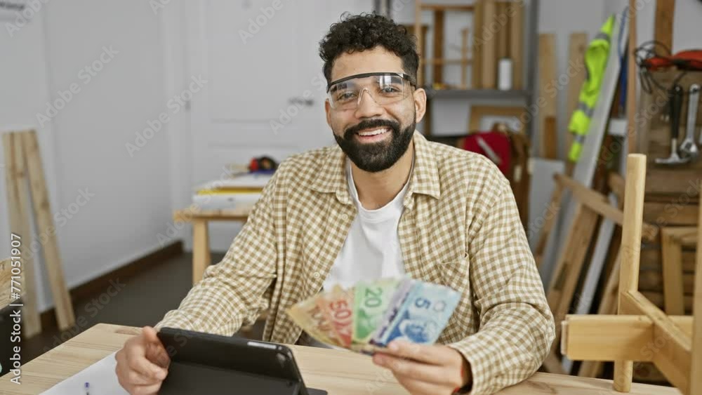 Handsome hispanic man counts canadian dollars in a carpentry workshop.