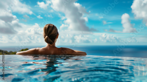 A woman relaxing in an rooftop pool overlooking the ocean, with a clear blue sky and white clouds, beautiful scenery.