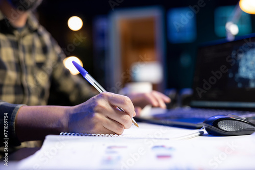 Selective focus of freelancer writing ideas and new code on a notebook to guarantee cyber security. Man managing programs in artificial intelligence and machine learning on a laptop.