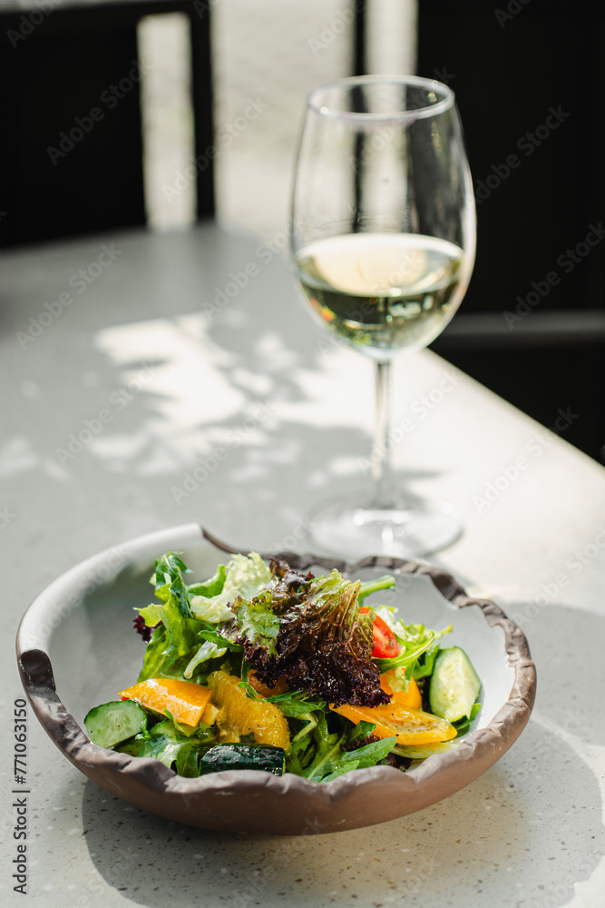 salad in a beautiful kitchen utensil and a glass of white wine outdoors on a white table