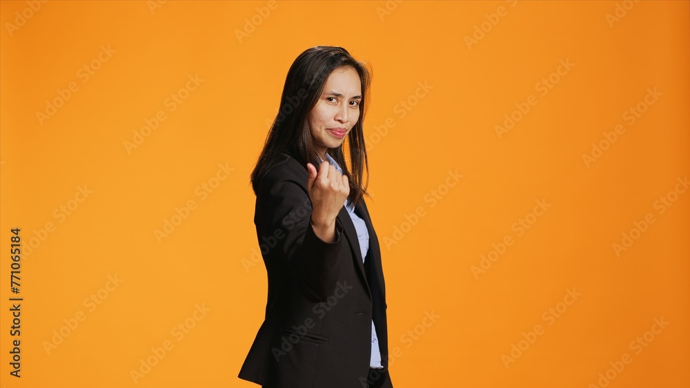 Proud business manager calling for someone in studio, doing hailing gesture with arm raised. Asian female model asking person to come here closer for a discussion against background. Proud business manager calling for someone in studio, doing hailing gesture with arm raised. Asian female model asking person to come here closer for a discussion against background.