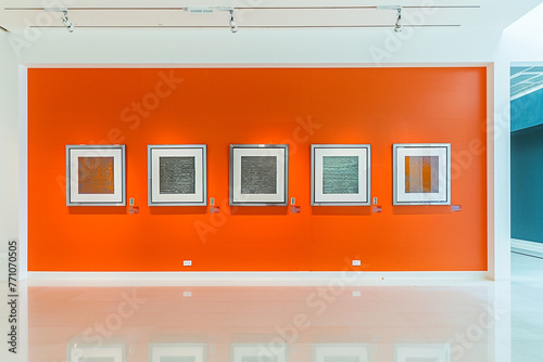 Inside a minimalist white art gallery  an orange wall pops with vibrancy. Silver frames