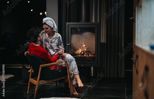 Intimate and warm scene of a couple in pajamas sharing a moment with a glass of wine near a glowing fireplace.