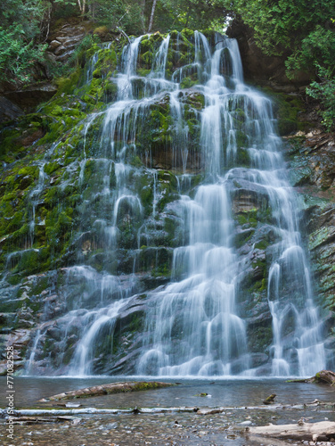 Scenic waterfall cascading gently over moss-covered rocks in a peaceful forest. Slow shutter speed creates a silky water effect. Serene natural landscape perfect for backgrounds.