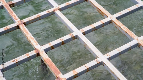 Metal grid construction above flowing water. Rusty steel frame - platform supporting structure above stream or river. Square geometric pattern. Corrosion protection.
