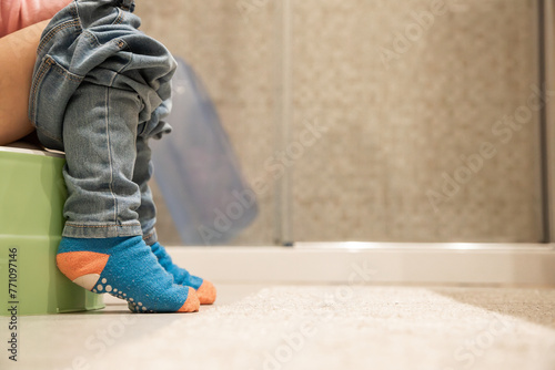 Small child sitting on plastic potty in bathroom. Concept of acquiring physiological skills. Close up and  copy space.