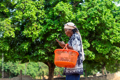 Young Female with Shopping Basket Using Phone, Side View, Green Leaves Background