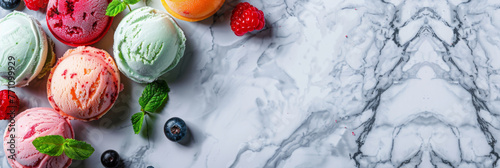 Top view of colorful ice cream scoops garnished with berries and mint leaves on a marble countertop