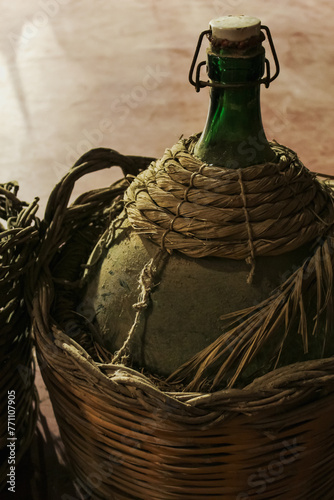 Foto Bottle of traditional Sicilian wine in a wicker basket, old/antique and dusty glass carboy, green wine bottle, demijohn vintage