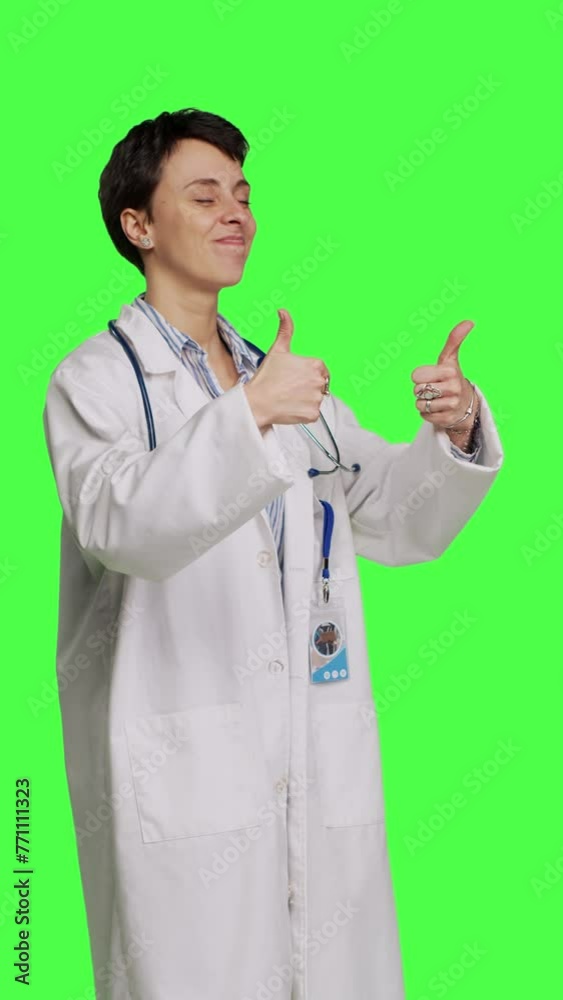 Side view Cheerful medic doing thumbs up symbol against greenscreen backdrop, expresses positivity with like sign. General practitioner with coat giving approval and being satisfied with success Side view Cheerful medic doing thumbs up symbol against greenscreen backdrop, expresses positivity with like sign. General practitioner with coat giving approval and being satisfied with success
