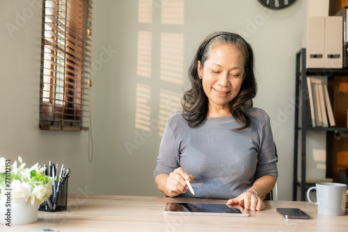 Elderly woman with glasses looking at digital tablet Concept of education, modern technology, casual woman sitting, relaxing, happiness. Surf the internet online