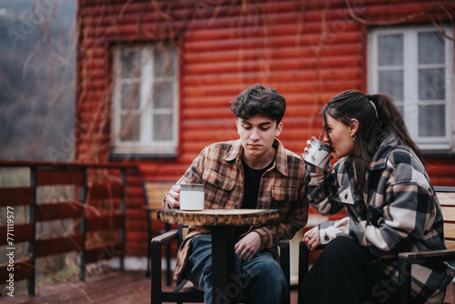 Young couple sits cozily on a porch, sharing intimate moments with a hot drink in a tranquil environment © qunica.com