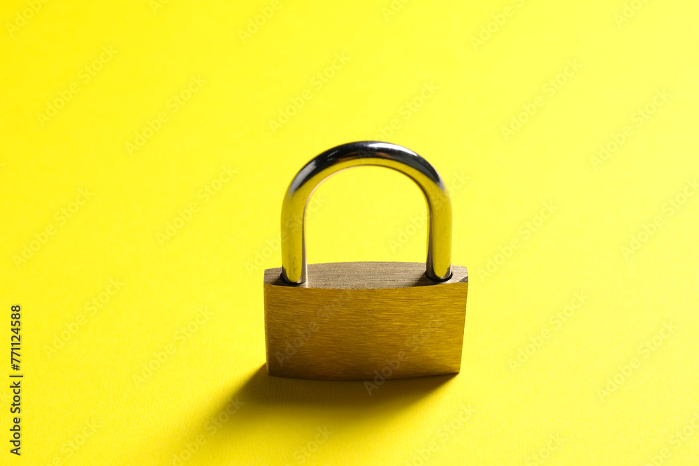 One locked steel padlock on yellow background One locked steel padlock on yellow background