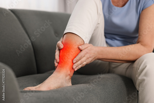 Arthritis symptoms. Woman suffering from pain in her leg on sofa indoors, closeup