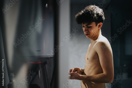 A contemplative young adult standing shirtless, bathed in soft light with a feeling of tranquility and introspection photo