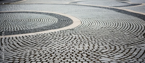 A detailed shot of a circular pattern created by Automotive tires on a grey cobblestone street, highlighting the unique road surface and geometric design