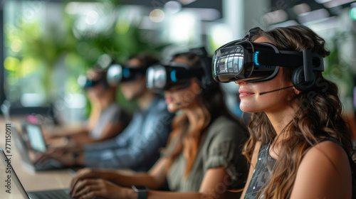A group wearing virtual reality headsets are sitting at a table. They are all focused on their laptops, possibly working on a project or playing a game. The atmosphere is focused and serious