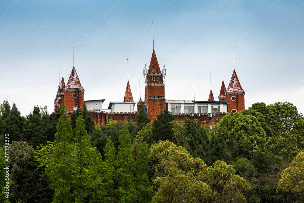 A group of ancient castle -style buildings are built in a small hillside forest, with a large lake outside, in a park in Deyang, China