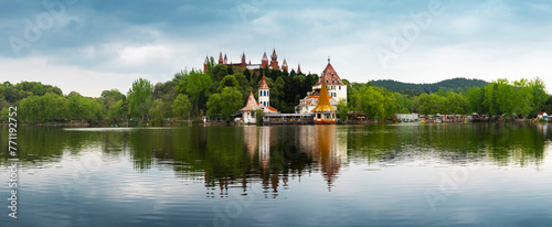 A group of ancient castle -style buildings are built in a small hillside forest, with a large lake outside, in a park in Deyang, China photo