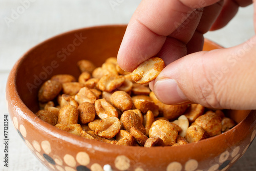 A closeup view of a hand grabbing roasted peanuts from a clay bowl.