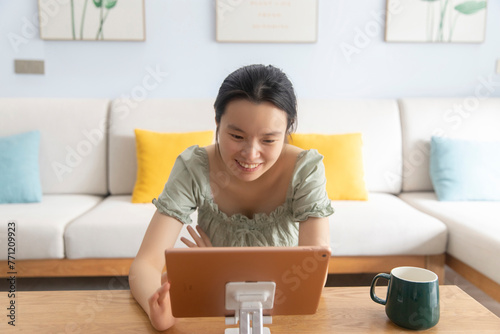 An Asian woman is in the living room at home, holding a tablet and watching TV for entertainment and learning