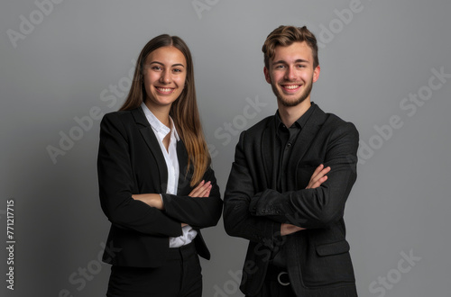 A photo of two professional young woman and man in black suit, arms crossed smiling on grey background with copy space for text