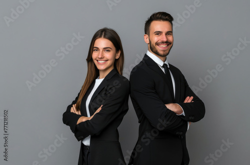 A photo of two professional young woman and man in black suit, arms crossed smiling on grey background with copy space for text