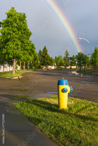 Yellow and blue color fire hydrant at city wet street after rain and rainbow