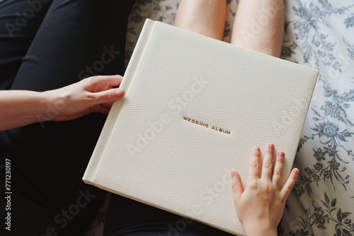 The hands are holding a wedding book in a white leather cover 