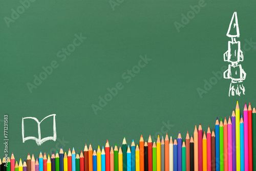 multicolored pencils on green chalkboard background, copy space, back to school concept and growth to knowledge, drawn book and rocket