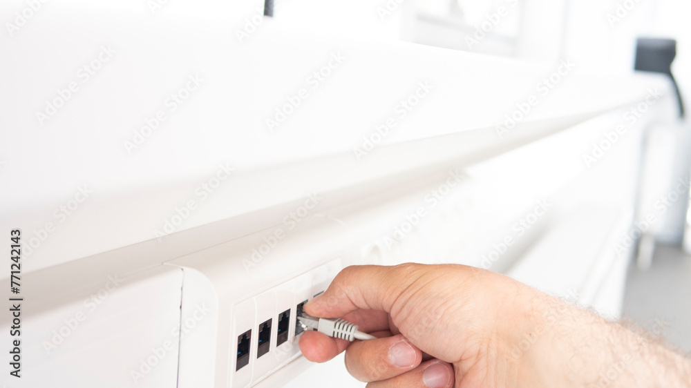 Patch cord with connectors RJ45. A man's hand plugs a power cord into an outlet in the white office. Patch cord with connectors RJ45. A man's hand plugs a power cord into an outlet in the white office.