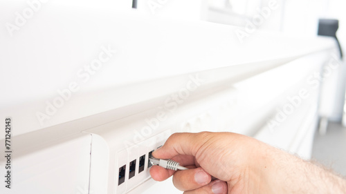 Patch cord with connectors RJ45. A man's hand plugs a power cord into an outlet in the white office.