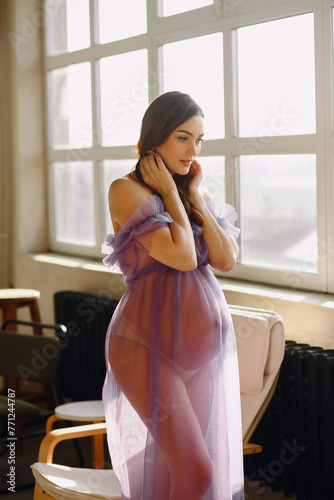 Beautiful pregnant woman in violet dress posing in the studio photo