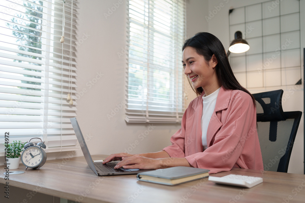 Beautiful young Asian woman working on laptop in home office Business woman sitting and typing Research information on the internet online at home in a relaxed and happy way.