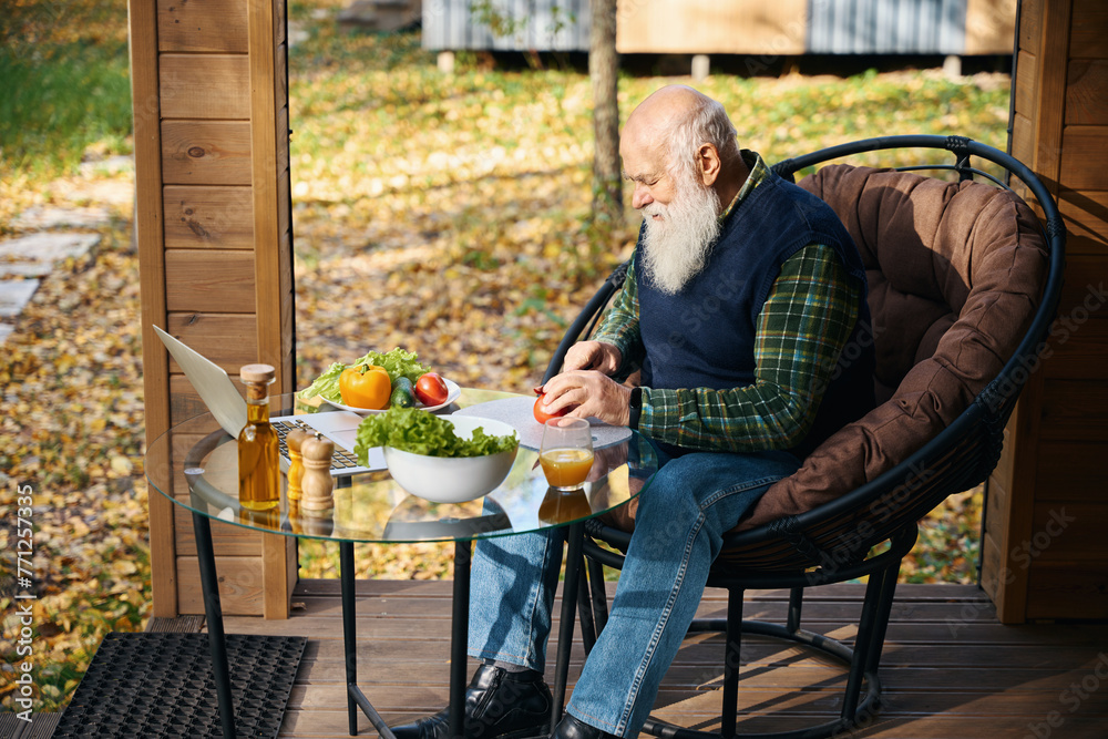 Pensioner sits on the veranda with breakfast and a laptop Pensioner sits on the veranda with breakfast and a laptop