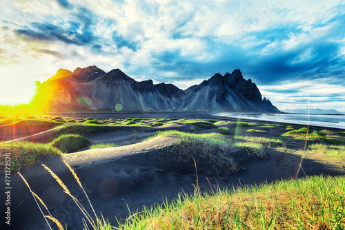 Dramatic sunny day and gorgeous rippled black sand beach and green grass on Stokksnes cape in Iceland. photo