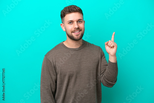 Young caucasian man isolated on blue background showing and lifting a finger in sign of the best