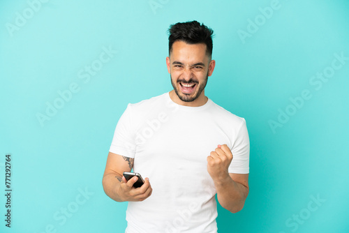 Young caucasian man isolated on blue background with phone in victory position
