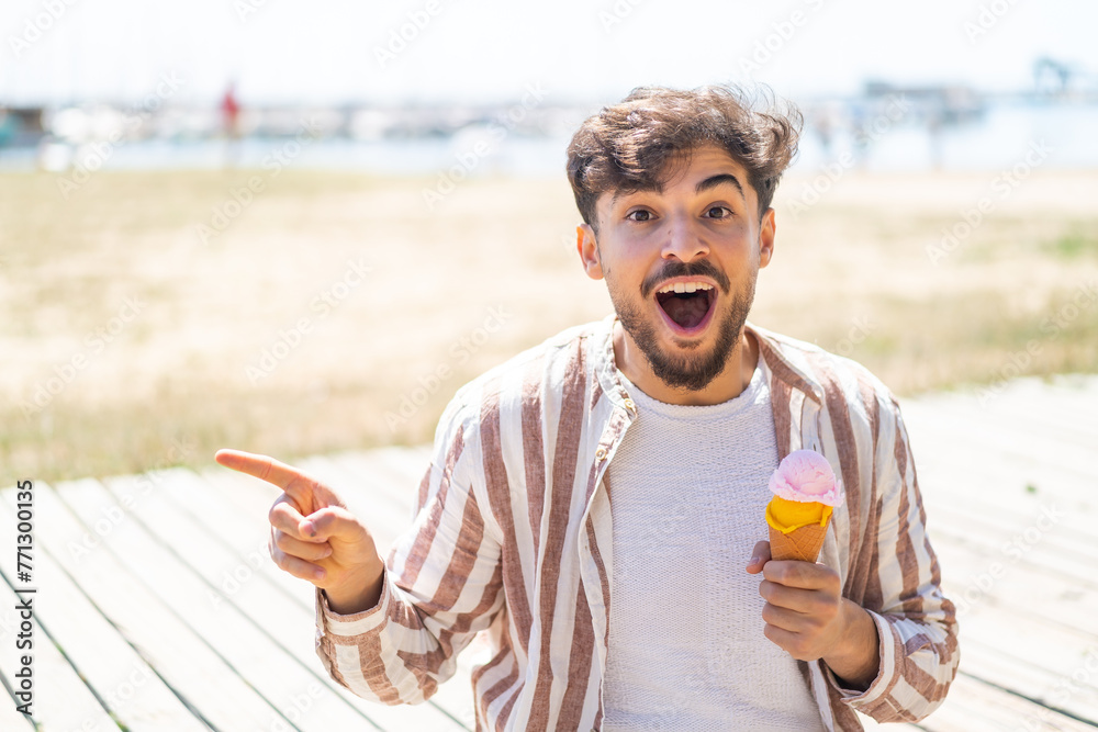Fototapeta premium Handsome Arab man with a cornet ice cream at outdoors surprised and pointing finger to the side