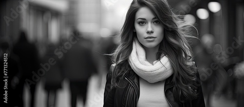 A young woman with a headscarf and flowing long hair walking gracefully along a city street in a monochrome urban setting
