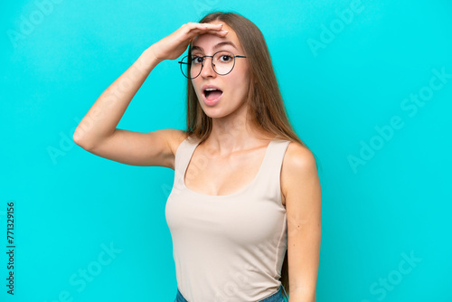 Young caucasian woman isolated on blue background doing surprise gesture while looking to the side