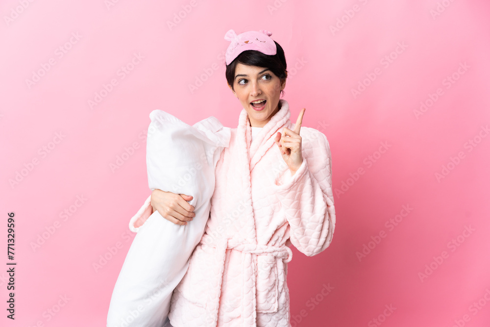 Woman with short hair isolated on pink background in pajamas and intending to realizes the solution while lifting a finger up