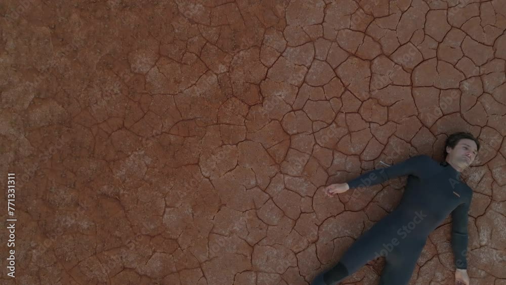 Drone clip of male model wearing wetsuit lying on cracked desert ground Drone clip of male model wearing wetsuit lying on cracked desert ground