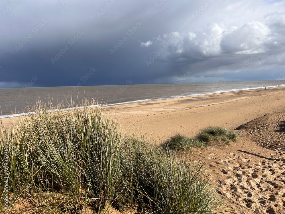 Man looking to ocean horizon beautiful sandy beach landscape grey stromy sky clouds and from grassy banks of sand dunes rolling waves on flat sea on Spring day in Winterton Norfolk East Anglia uk  - obrazy, fototapety, plakaty 