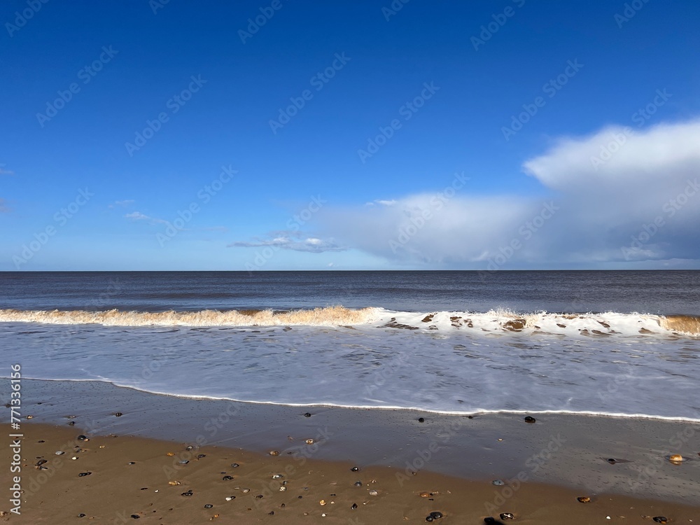 Beautiful landscape view of the vast sandy beach in Norfolk East Anglia uk with clear blue skies white cloud storm approaching calm rolling waves of sea and no people Beautiful landscape view of the vast sandy beach in Norfolk East Anglia uk with clear blue skies white cloud storm approaching calm rolling waves of sea and no people