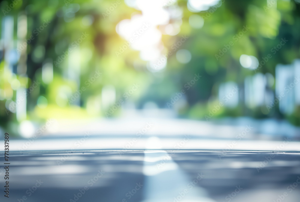 Blurred background of an outdoor scene with white and green colors, blurred focus on a road in the foreground. The blurry urban landscape is adorned with lush trees. - obrazy, fototapety, plakaty 