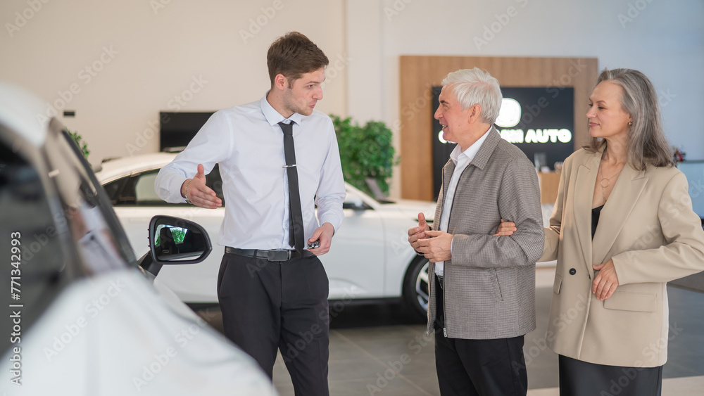 Obraz premium A salesman in a car dealership shows a car to a mature married couple.
