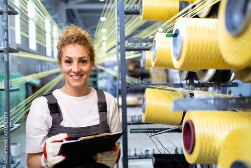 Female worker checking on industrial knitting machine inside textile factory. photo