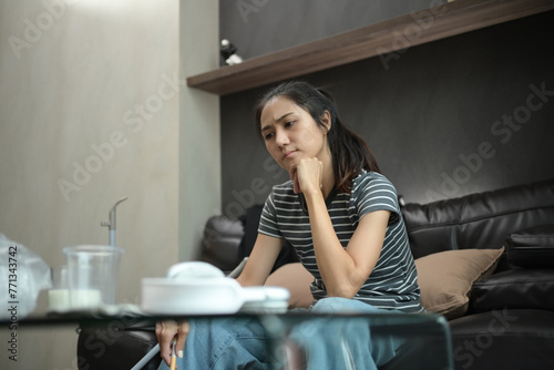 Tired and upset young woman sitting on sofa in messy room